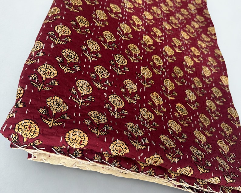 Puede incluir: Textil granate doblado con un patr&oacute;n repetido de dise&ntilde;os florales amarillos. La tela est&aacute; cosida con hilo blanco y los bordes son de color beige claro.
