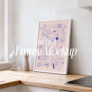 May include: White framed art print featuring a pink background with blue line drawings of kitchen-related items. The print includes illustrations of food, drinks, and utensils. Text on the print reads "Kitchen Frame Mockup" and "Mockup no. 477".
