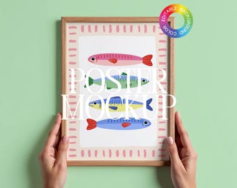 Op de afbeelding: Een ingelijste poster met vier kleurrijke visillustraties. De vissen zijn roze, groen, geel en blauw, elk met rode vinnen. De poster heeft een lichte houten lijst en een witte achtergrond met roze accenten. De tekst "POSTER MOCKUP" is over de afbeelding geplaatst.