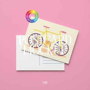 Könnte beinhalten: Ein Postkarten-Mockup mit einer Fahrradillustration in Gelb, Lila und Orange auf cremefarbenem Hintergrund. Die Worte "POSTCARD MOCKUP" sind weiß gedruckt. Darunter befindet sich eine leere Postkarte, alles auf rosa Hintergrund.
