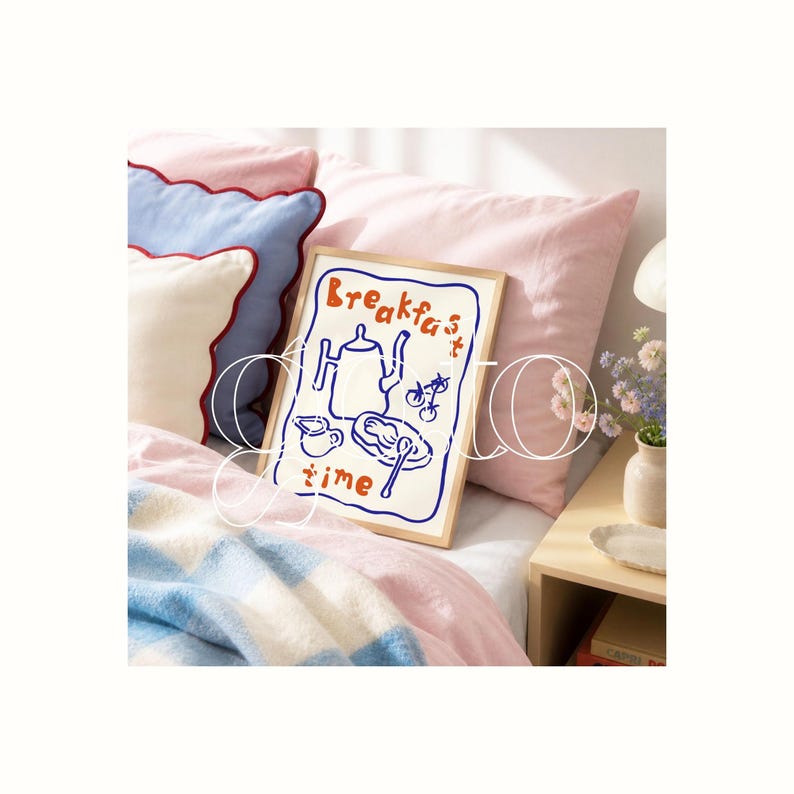 Op de afbeelding: Een ingelijste print met de woorden "Breakfast time" in oranje en blauw. De illustratie toont een theepot, een kopje, een bord met eten en bestek. De print ligt op een bed met roze en blauwe kussens en een patroon deken.