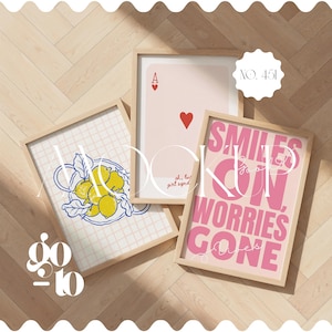 May include: Three framed art prints with light wood frames. One print features a lemon design, another an Ace of Hearts playing card, and the third reads "Smiles on, worries gone." The prints are displayed on a light wood floor.