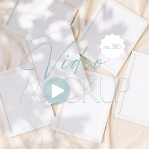 May include: A collection of white picture frames arranged on a beige surface. The frames are rectangular with a simple, clean design. The image includes the text "Video MOCKUP" in a light blue script, along with a play button icon and the number "no. 385".