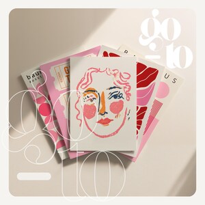 May include: A stack of art prints featuring abstract illustrations and the text "go to". The prints showcase a variety of designs, including a face with pink and orange accents, and other abstract shapes in pink and red. The background is a soft, neutral color.