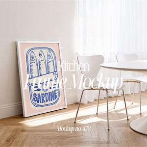 Op de afbeelding: Een ingelijste kunstprint met een sardineblik-illustratie in blauw en wit op een roze achtergrond. De print zit in een witte lijst en leunt tegen een muur. De tekst "SARDINE" is zichtbaar op het blik. Keuken frame mockup.
