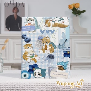 May include: A notebook with a blue and white checkered pattern, decorated with cartoon cats in various poses and costumes. The notebook has text that says "small steps every day" and "progress, not perfection.". The notebook is approximately 20 cm in height.