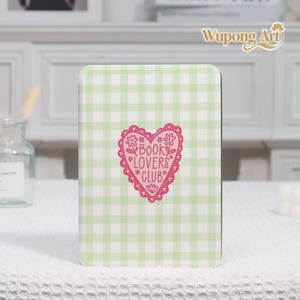 May include: A rectangular notebook with a green and white gingham pattern. A pink heart-shaped graphic with the words "BOOK LOVERS CLUB" is centered on the cover. The notebook is a book-themed item.