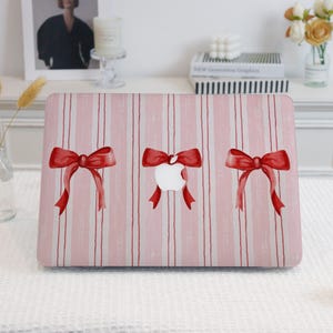 May include: Pink and white striped laptop skin with three red bows. Each bow has a white apple in the center.