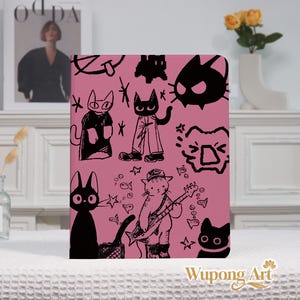 May include: A pink notebook featuring black cat illustrations in various poses. One cat plays a guitar, while others are depicted with stars and fish. The notebook has a simple, artistic design.
