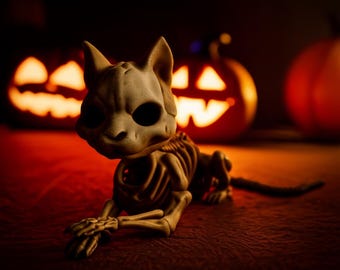 Pode incluir: Uma estatueta de esqueleto de gato bege com grandes órbitas oculares pretas, posada sobre uma superfície vermelha. Duas lanternas de abóbora iluminadas estão no fundo, criando um tema de Halloween. A caixa torácica e a coluna vertebral do gato são visíveis.