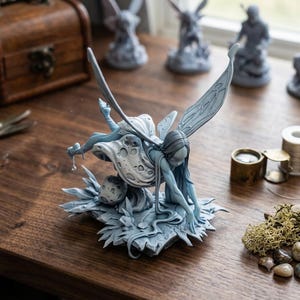 May include: A light blue, unpainted resin figurine of a fairy with long hair and large, detailed wings. The fairy is depicted in a crouching position, resting on a base decorated with foliage and a small, cratered moon-like sphere.