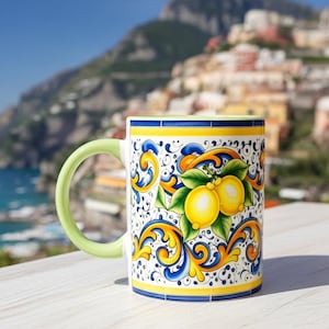 Peut inclure: Une tasse en c&eacute;ramique orn&eacute;e d'un motif vibrant de citrons jaunes avec des feuilles vertes, entour&eacute;s de volutes bleues et jaunes complexes. La tasse poss&egrave;de une anse vert clair unie, un int&eacute;rieur blanc et une bordure jaune et bleue.