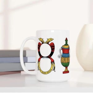 A white mug with colorful illustrations of a vase and a snake on it, placed on a white surface.