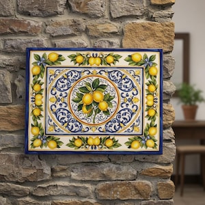 May include: A rectangular ceramic tile featuring a central circular medallion with a lemon branch, surrounded by intricate blue and yellow scrollwork patterns. The border is decorated with a repeating motif of yellow lemons and green leaves.