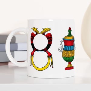 May include: White ceramic mug with a red, yellow, and black design of two birds and a vase. The vase is green, red, yellow, and blue with a gold trim. The text "Made in Italy" is printed on the mug.