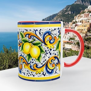Peut inclure: Un mug en c&eacute;ramique orn&eacute; d'un motif color&eacute; de citrons jaunes et de feuilles vertes sur fond blanc, agr&eacute;ment&eacute; de volutes bleues et jaunes. Ce mug pr&eacute;sente une anse rouge unie ainsi qu'un bord rouge, mettant en valeur un d&eacute;cor peint d&eacute;taill&eacute;.