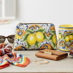 Op de afbeelding: Een verzameling accessoires met een citroenmotief. De afbeelding toont een etui met ritssluiting, een mok, een portemonnee, een sjaal, een zonnebril en een armband. De etui en mok hebben een witte achtergrond met gele citroenen, groene bladeren en blauwe en oranje patronen.