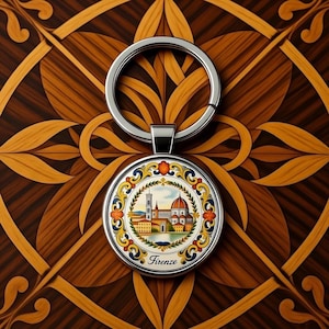 May include: A silver keychain with a round pendant featuring a colorful illustration of a cityscape with a cathedral and the word "Firenze". The keychain is set against a decorative wooden background.