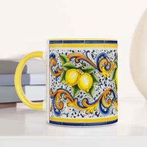 Peut inclure: Un mug en c&eacute;ramique avec une anse jaune vif et un motif d&eacute;coratif de citrons jaunes &eacute;clatants avec des feuilles vertes, sur fond blanc avec des volutes bleues et jaunes complexes et des bandes de bordure horizontales.