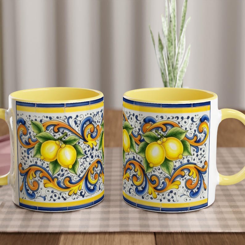 Peut inclure: Deux tasses en c&eacute;ramique orn&eacute;es d'un motif de citrons jaunes avec des feuilles vertes sur fond blanc. Le design comprend des bordures complexes &agrave; volutes bleues et orange. Chaque tasse poss&egrave;de un int&eacute;rieur jaune uni et une anse jaune.