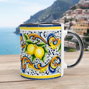 Peut inclure: Un mug en c&eacute;ramique blanche orn&eacute; d'un motif vibrant de citrons jaunes avec des feuilles vertes, entour&eacute; de volutes complexes bleues et jaunes. Le mug pr&eacute;sente un int&eacute;rieur blanc lisse, une finition brillante et une anse lat&eacute;rale robuste.