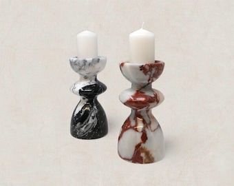 May include: Two marble candle holders with white candles. One is black and white, the other is white and red. The candle holders have a unique, stacked design. The candles are white and cylindrical.