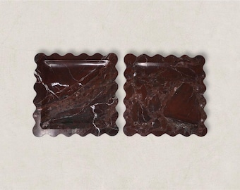 May include: Two square, decorative trays with a wavy edge. The trays are made of a dark red marble with white veining. The trays are empty and sit on a light background. These trays are ideal for serving appetizers or displaying small items.