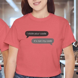 May include: Two people wearing coral-colored t-shirts with the text "I stole your code" above "it's not my code" in speech bubbles. The shirts are paired with blue jeans. The background shows an office setting.