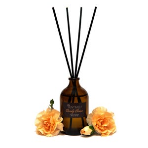 Pode incluir: Uma garrafa de vidro marrom com varetas difusoras pretas e um rótulo que diz "Sentimelt Candy Coma Home Fragrance 200 ml - 6.7 fl oz". A garrafa é cercada por três flores amarelas.