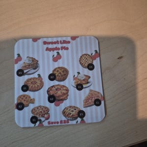 May include: A square coaster with a pink and white striped background features illustrations of various apple pies. The text "Sweet Like Apple Pie" is at the top. The coaster has a cherry design and the text "Save £25".