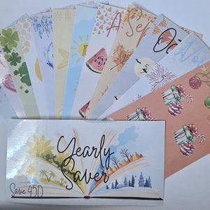 Pode incluir: Um conjunto de envelopes de orçamento ilustrados, cada um representando um mês do ano. Os envelopes apresentam designs sazonais, incluindo uma melancia, folhas de outono e enfeites de Natal. Um envelope maior na parte inferior diz "Yearly Saver".