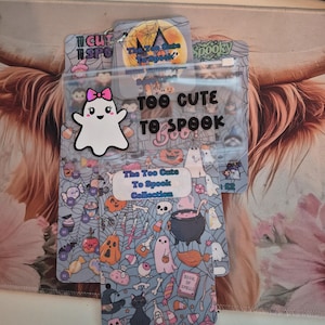 May include: Transparent plastic pouches with Halloween designs. One pouch features a ghost with a pink bow and the text "TOO CUTE TO SPOOK." The other pouch has a pattern of ghosts, pumpkins, and cats. The text "The Too Cute To Spook Collection" is also visible.