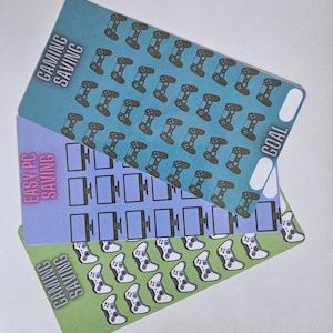 May include: Three colorful gaming-themed saving goal cards. The top card is blue with brown game controllers and the text "GAMING SAVING". The middle card is purple with computer monitor graphics and the text "EASY PC SAVING". The bottom card is green with white game controllers.