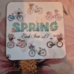 May include: A white coaster with a spring theme, featuring bicycles with flower baskets and the word "SPRING" in green and blue. The text "Each Icon L1" is also present.