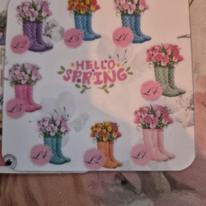 May include: A sticker sheet with illustrations of wellington boots filled with tulips. The boots are in various colours, including purple, blue, pink, and orange. The words "Hello Spring" are written in pink script.