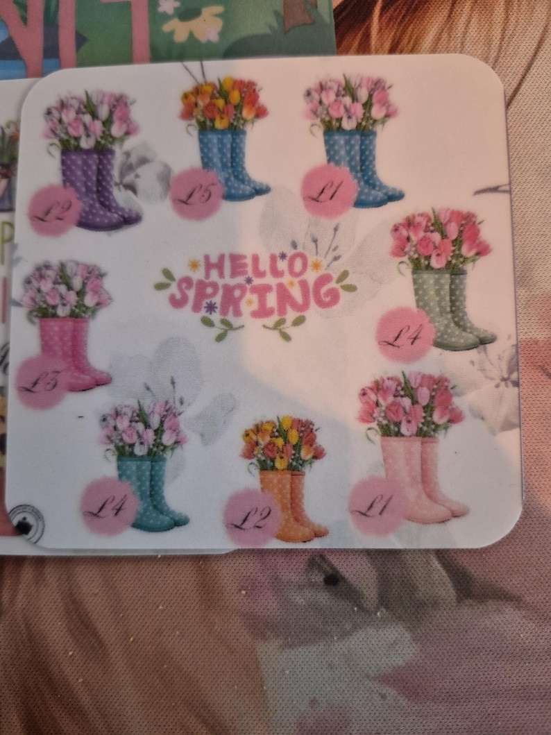 May include: A sticker sheet featuring colorful illustrations of rain boots filled with tulips. The boots are in various colors, including purple, blue, pink, and orange. The words "Hello Spring" are written in pink script.