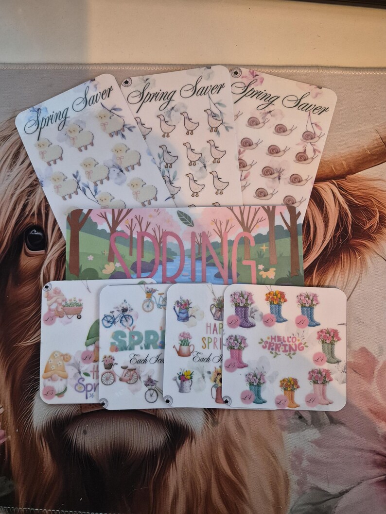 May include: A collection of spring-themed cards with various designs. Some cards feature sheep, ducks, and snails, while others display gnomes, bicycles, and flower-filled boots. The word "SPRING" is prominently displayed on several cards.
