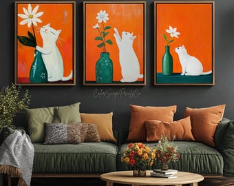 May include: Three framed art prints featuring white cats interacting with flowers in vases against an orange background. The artwork has a whimsical, illustrative style, with a wooden frame. The prints are displayed above a green sofa with orange and green pillows.
