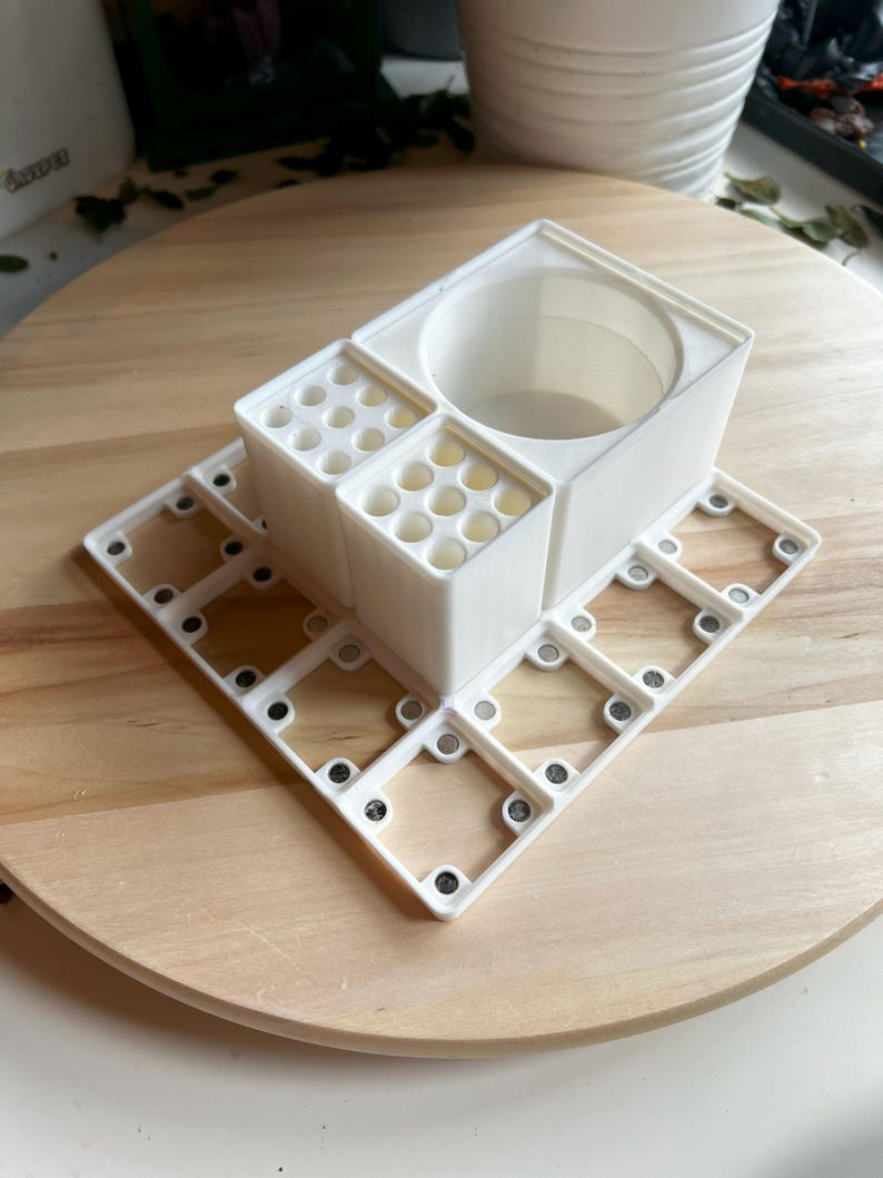 Puede incluir: Organizador de escritorio de pl&aacute;stico blanco con m&uacute;ltiples compartimentos, incluyendo una taza redonda, y una base cuadrada con cierres magn&eacute;ticos.