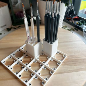 Puede incluir: Portacepillos de pintura de pl&aacute;stico blanco con una cuadr&iacute;cula de 20 cuadrados peque&ntilde;os. El portacepillos tiene dos compartimentos verticales para cepillos. Un compartimento contiene 10 cepillos negros y el otro compartimento contiene 3 cepillos blancos.