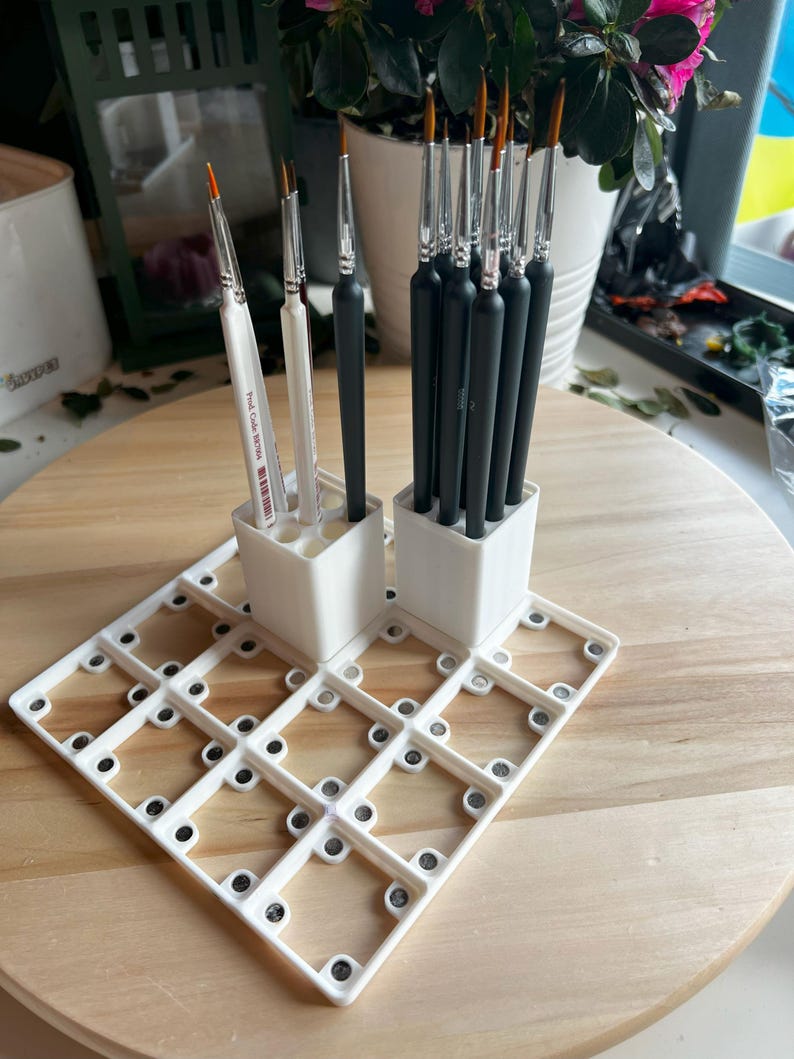 Puede incluir: Portacepillos de pintura de pl&aacute;stico blanco con una cuadr&iacute;cula de 20 cuadrados peque&ntilde;os. El portacepillos tiene dos compartimentos verticales para cepillos. Un compartimento contiene 10 cepillos negros y el otro compartimento contiene 3 cepillos blancos.
