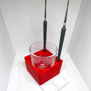 May include: Red plastic paintbrush holder with a glass jar and two paintbrushes. The holder has a white base with four compartments.