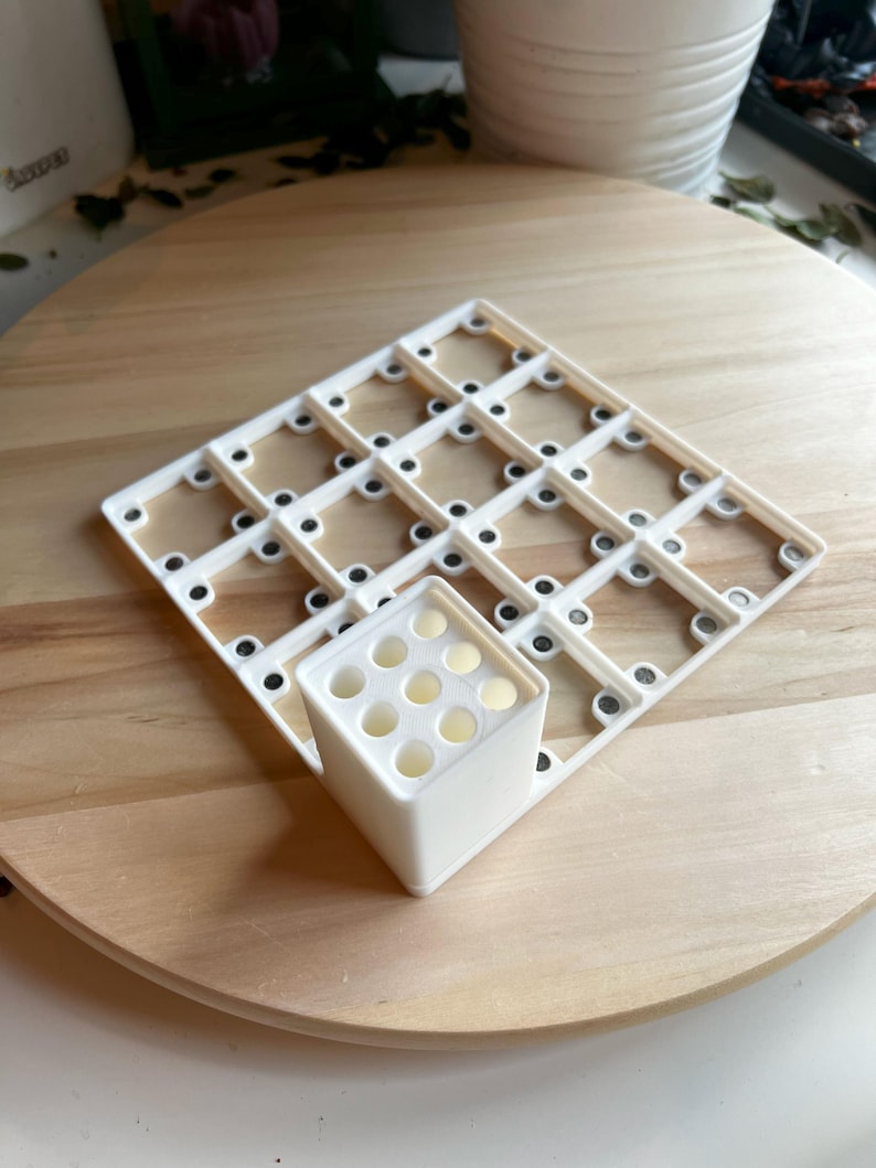 Puede incluir: Rejilla de pl&aacute;stico blanco con peque&ntilde;os c&iacute;rculos negros y un cubo de pl&aacute;stico blanco con nueve agujeros. La rejilla y el cubo est&aacute;n sobre una superficie de madera.