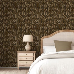 May include: A bedroom scene featuring wallpaper with a repeating dark brown and tan leaf pattern. A wooden nightstand with three drawers supports a beige lamp with a fabric shade. A bed with a light wood frame and white bedding is visible.