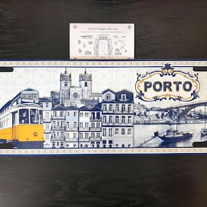Könnte beinhalten: Ein rechteckiges dekoratives Metallschild mit einer blau-weißen Illustration der Stadtansicht von Porto, einschließlich einer gelben Straßenbahn, dem Clérigos-Turm und der Dom-Luis-I-Brücke. Das Wort PORTO steht in einem Rahmen rechts.