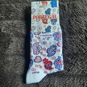 May include: White socks with a Portuguese design featuring red and blue paisley patterns and the word "PORTUGAL". The socks are size 9-11 and are displayed on a gray, textured surface.