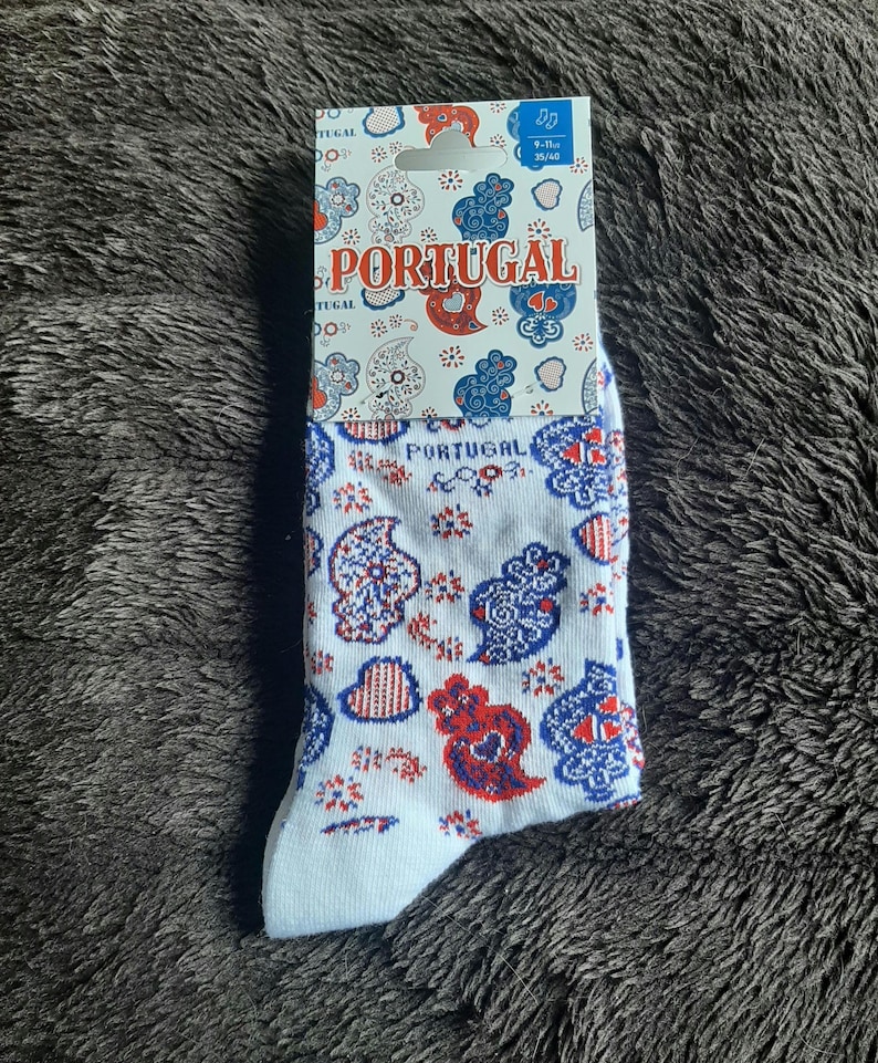 May include: White socks with a Portuguese design featuring red and blue paisley patterns and the word "PORTUGAL". The socks are size 9-11 and are displayed on a gray, textured surface.