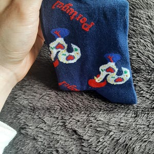 May include: Navy blue socks with a repeating pattern of a white and red design, with the word "Portugal" in red. The socks are held by a hand.