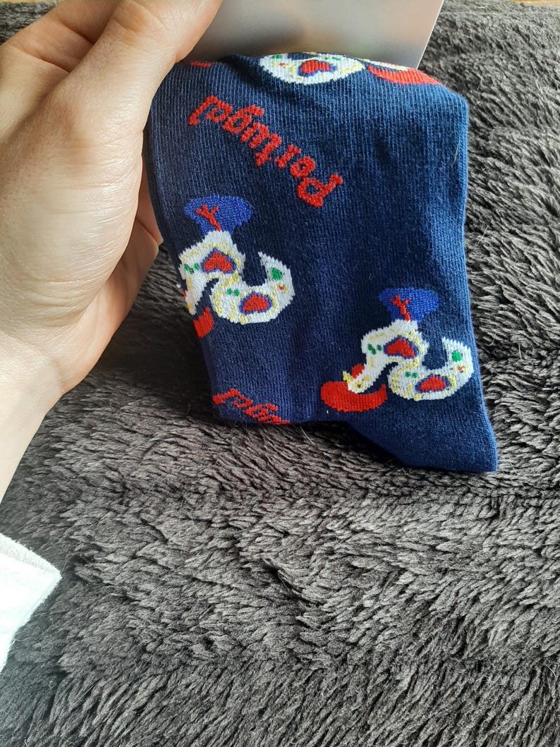 May include: Navy blue socks with a repeating pattern of a white and red design, with the word "Portugal" in red. The socks are held by a hand.