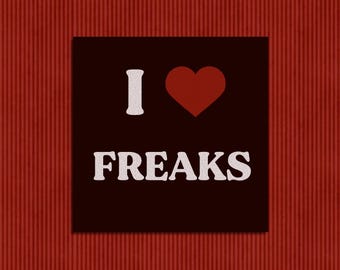 May include: A square black sign featuring the white text I, a red heart symbol, and the white text FREAKS centered below. The design uses a bold, rounded font for the lettering, creating a high-contrast graphic display on a dark background.